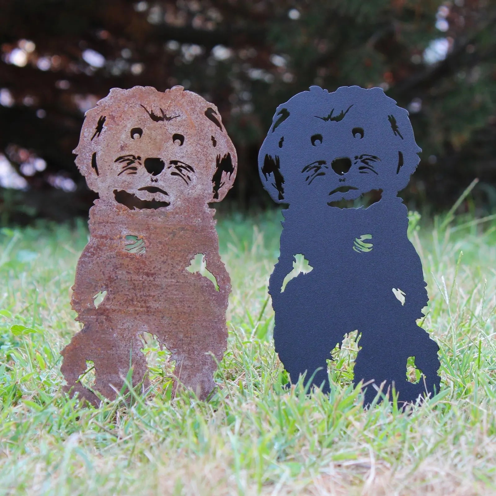 Rusty corten steel and black metal Maltese dog silhouettes stand in grass, showcasing durable outdoor dog decor.