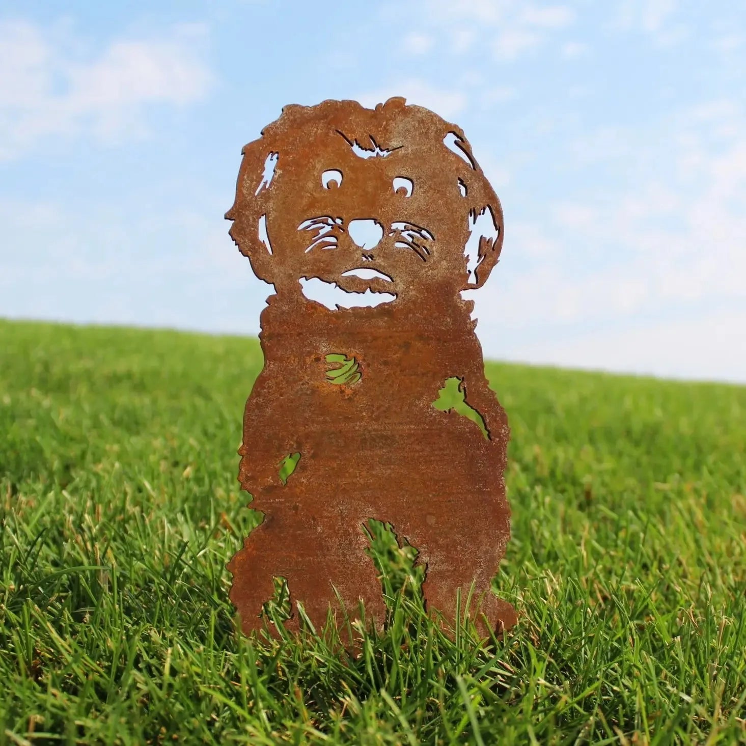 Rusty metal Maltese silhouette standing on green grass under a blue sky, ideal for outdoor dog decor.