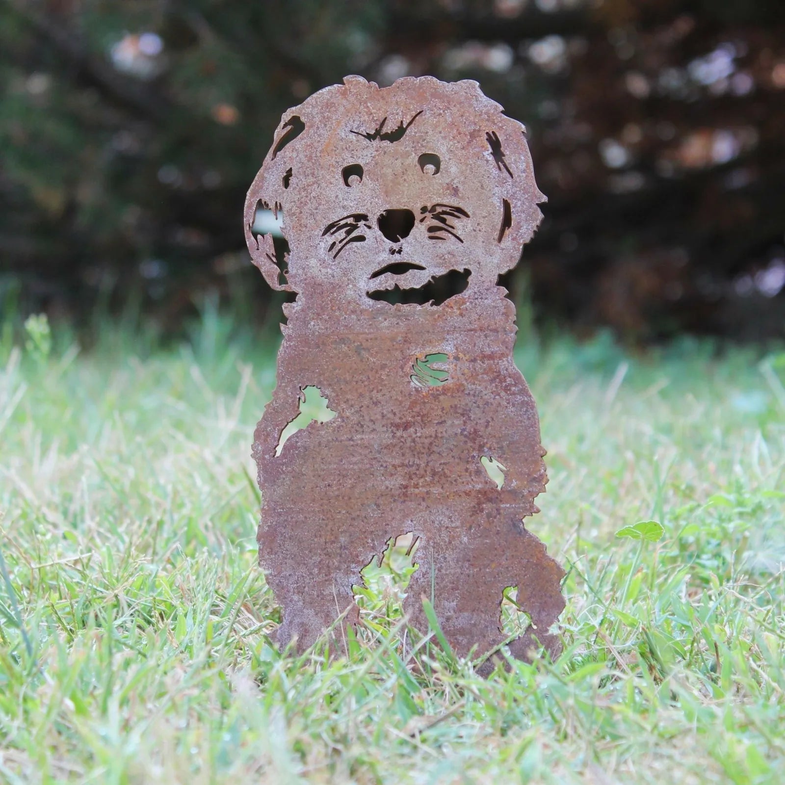 Rusty metal silhouette of a Maltese dog, standing in grass, showcasing a weathered Corten steel finish.