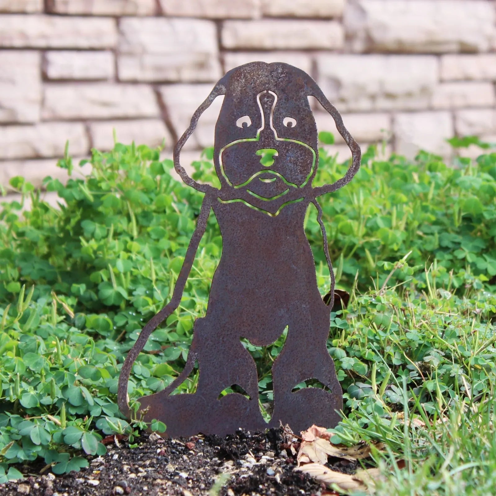 Maltipoo metal silhouette in weathered steel, set against green grass and a stone backdrop, perfect for outdoor decor.