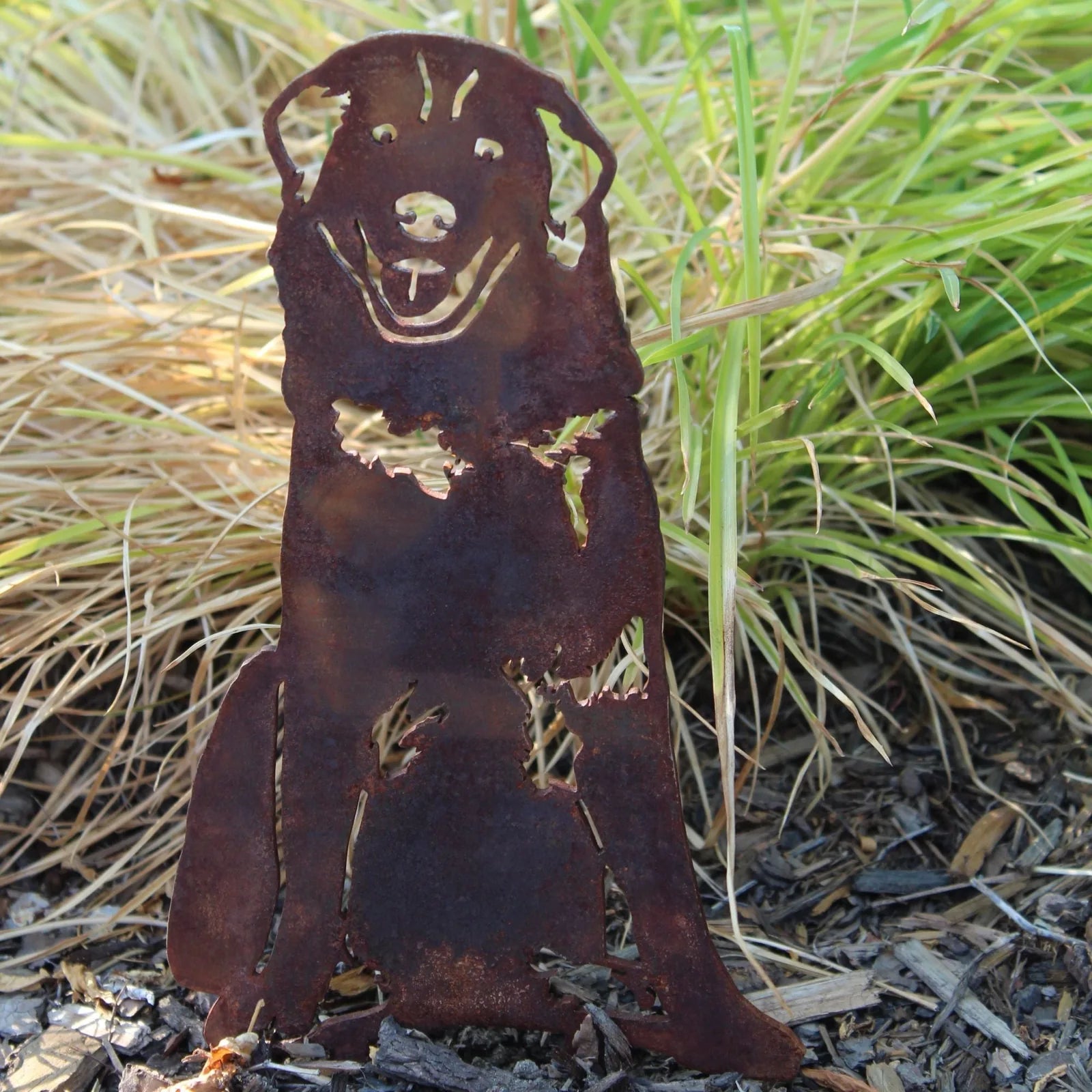 Rusty metal silhouette of a Maremma Sheepdog sitting, surrounded by grass and mulch, showcasing its playful design.