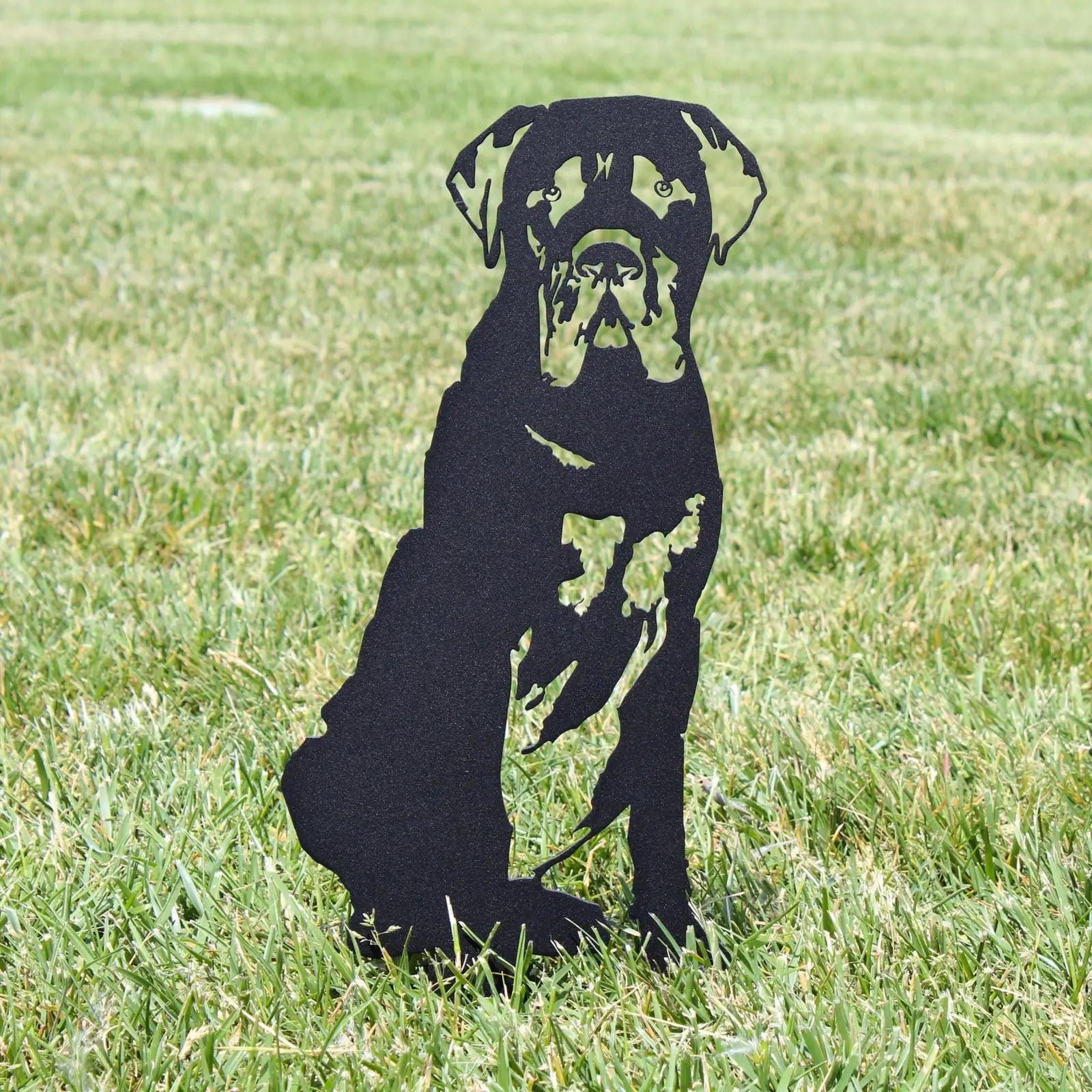 Black metal silhouette of a seated Mastiff, set against a grassy outdoor background.
