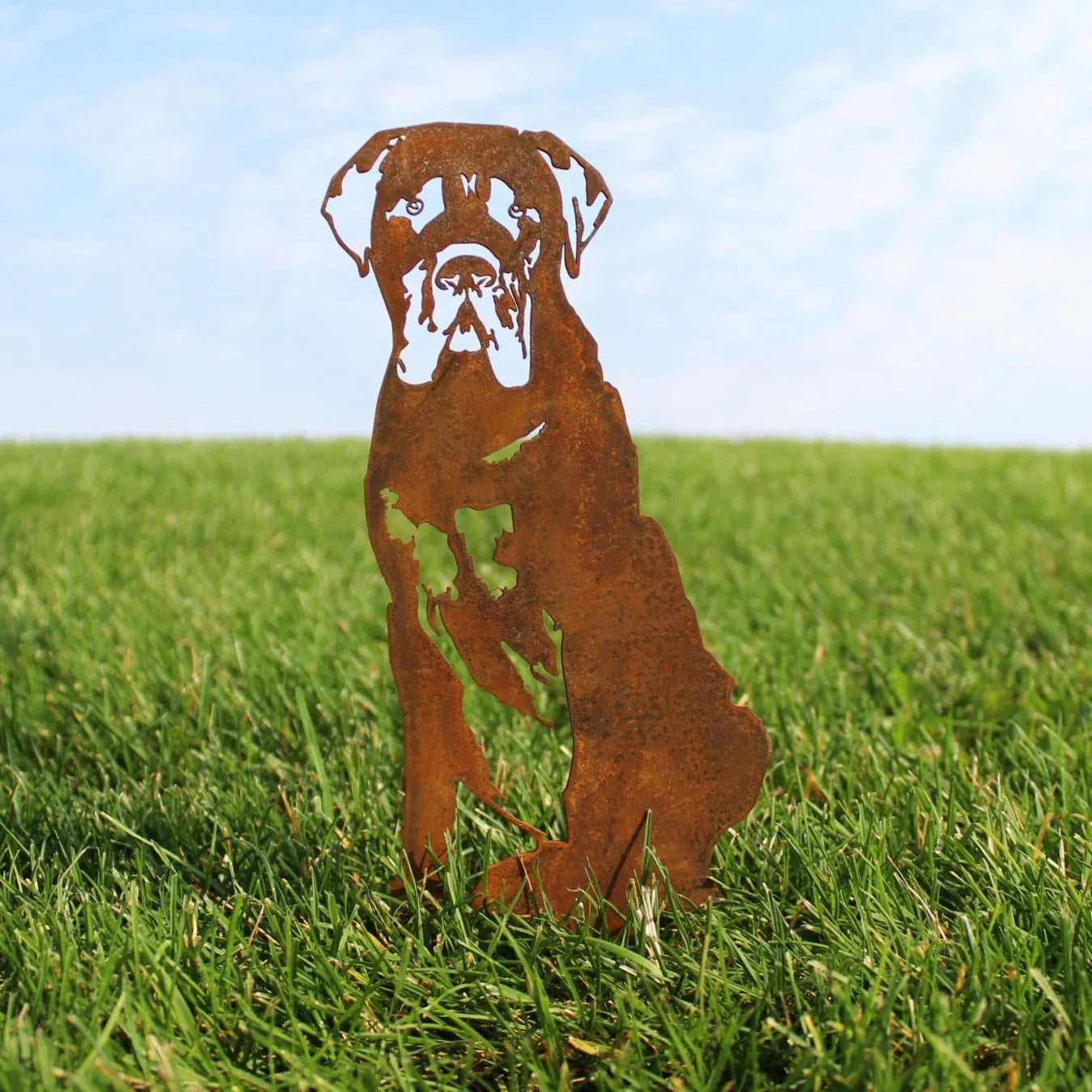 Rusty Corten steel silhouette of a seated Mastiff, set against a grassy background and blue sky.