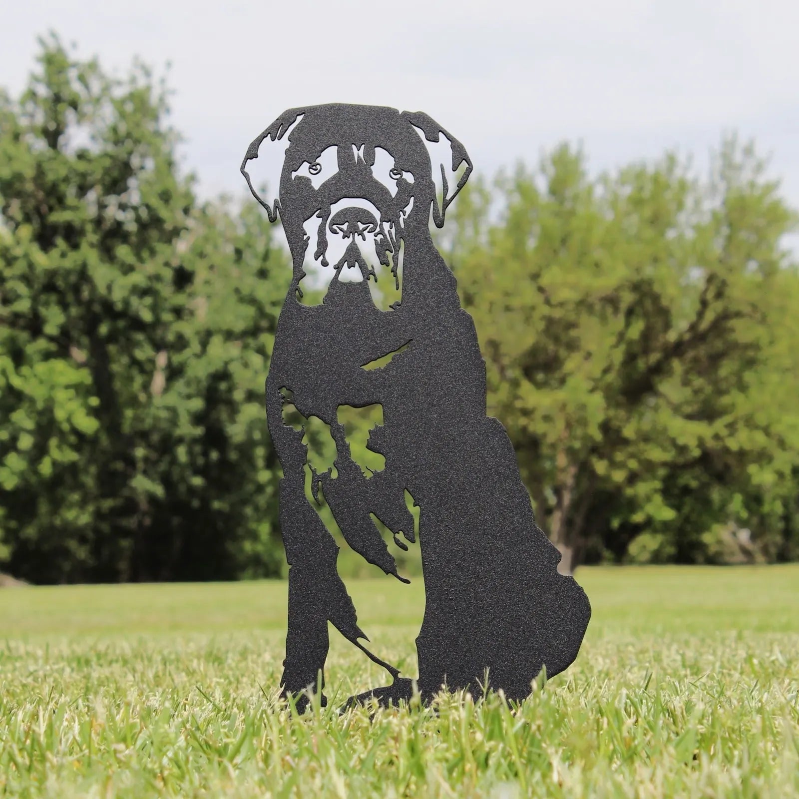 Black metal silhouette of a seated Mastiff in a grassy outdoor space, showcasing detailed craftsmanship.