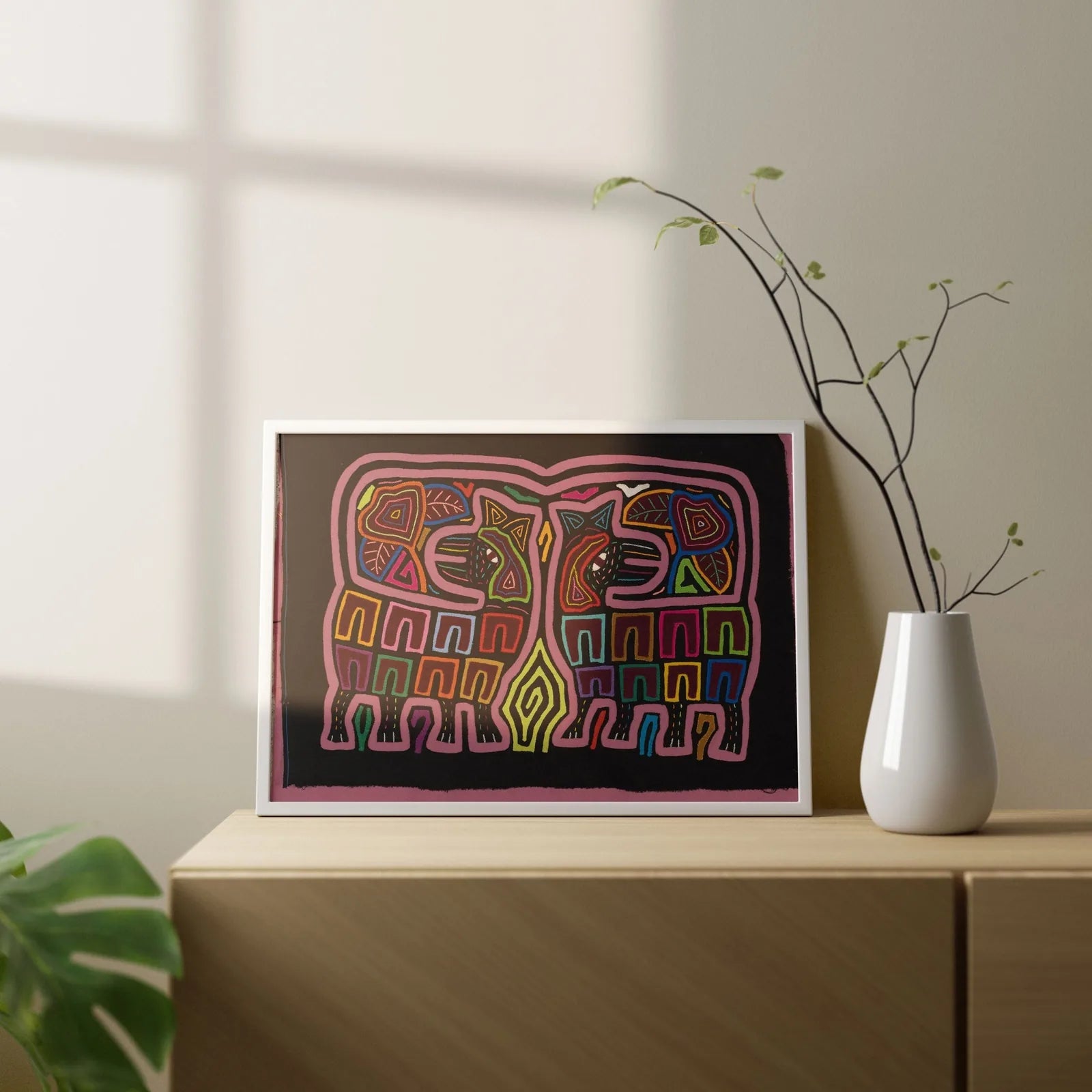 Colorful hand-stitched Mola featuring geometric animal patterns on a black background, framed and displayed on a wooden su...