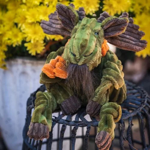 Cuddly Milo Moose plush dog toy in green corduroy with knotted limbs, surrounded by yellow flowers.