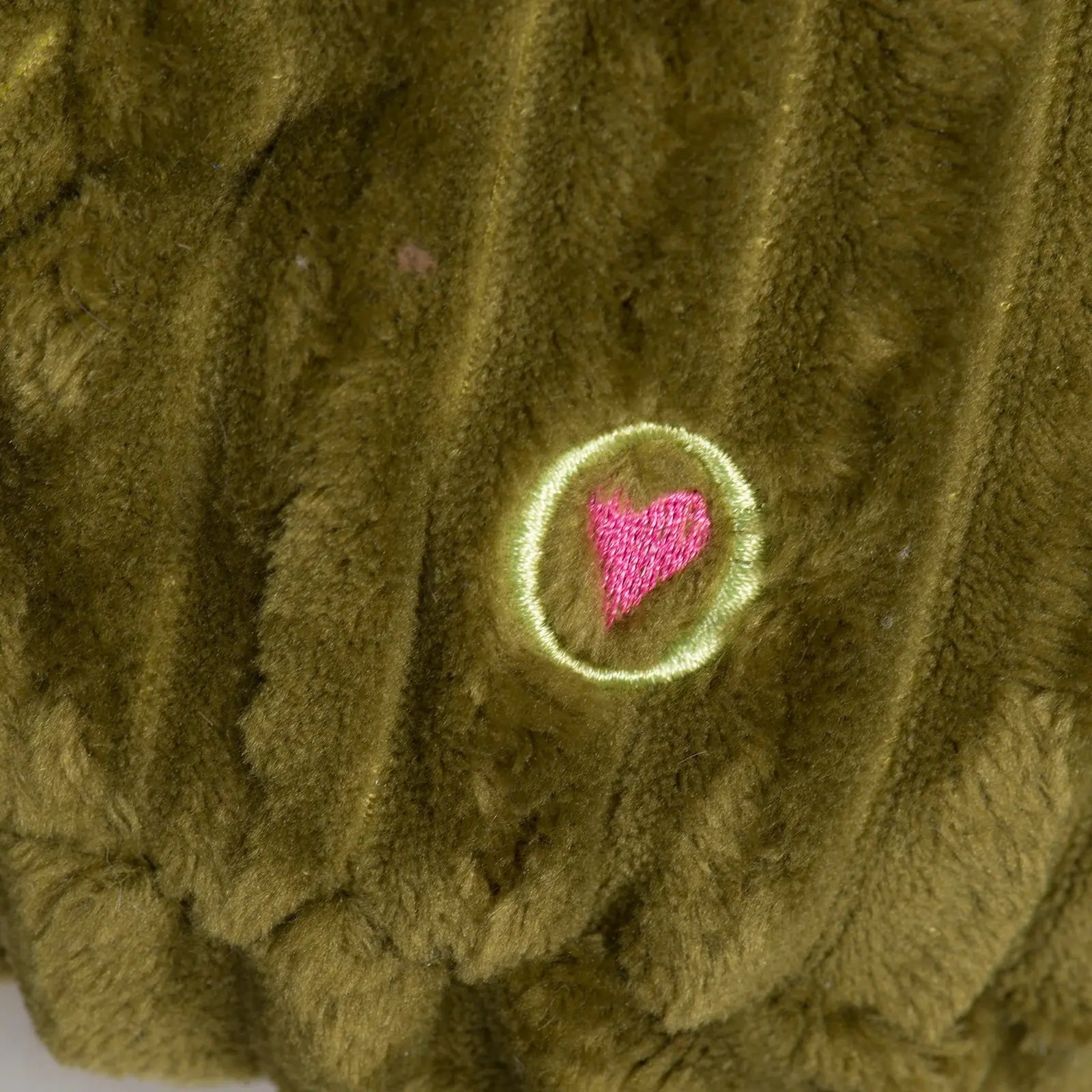 Close-up of Milo Moose plush toy showing soft green corduroy and an embroidered pink heart logo.