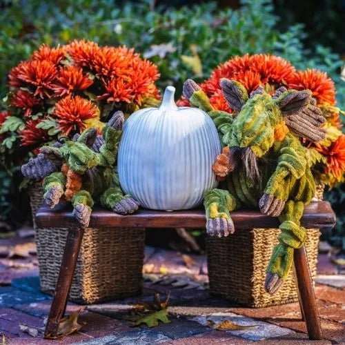 Cuddly Milo Moose plush dog toy with knotted limbs, surrounded by autumn flowers and a decorative pumpkin on a wooden bench.