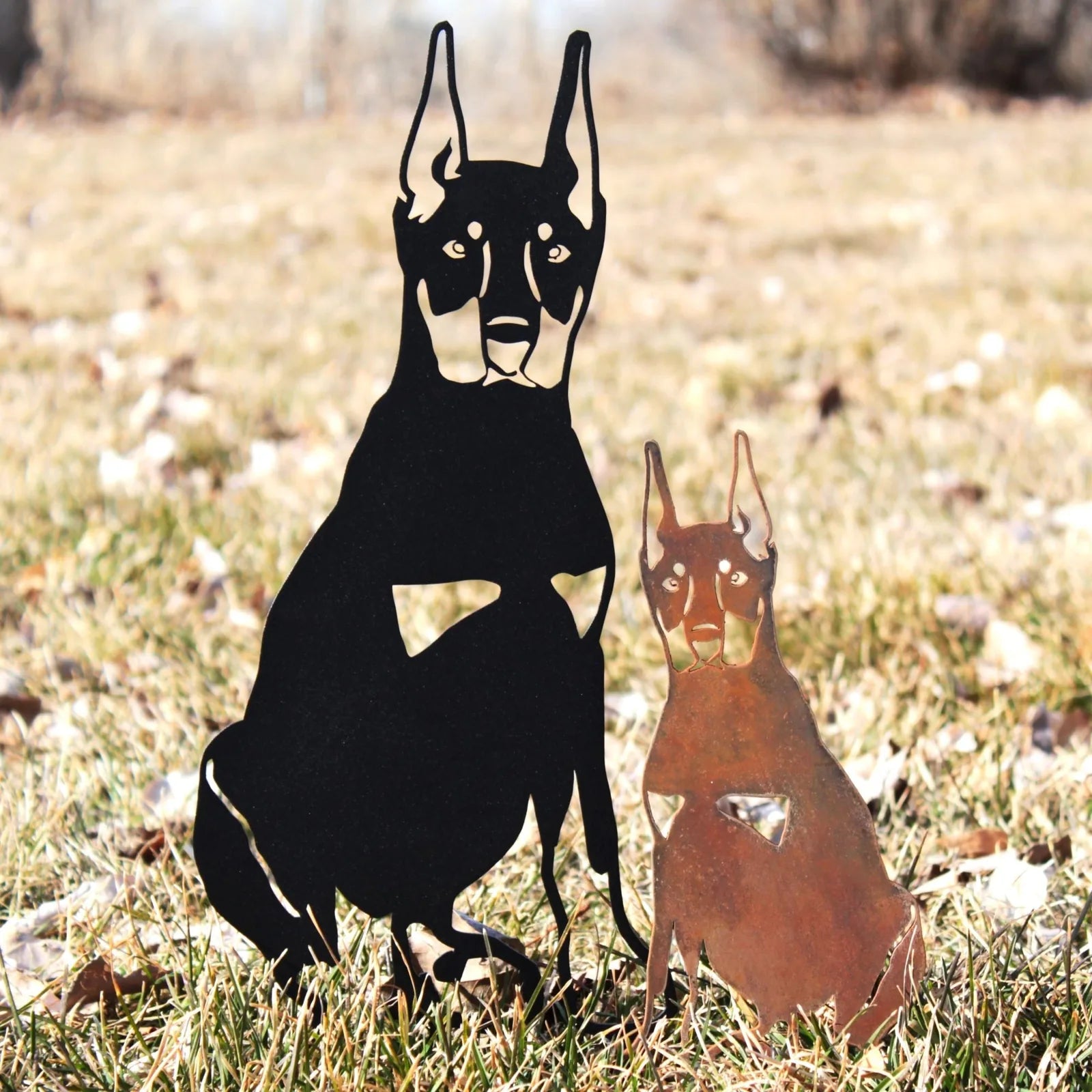 Miniature Pinscher metal silhouettes in black and rust, set against grass, showcasing outdoor dog decor by My Metal Rescue.