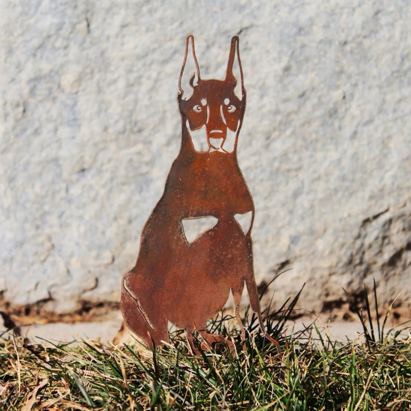 Miniature Pinscher metal silhouette in rust patina, set on grass with stone backdrop, showcasing outdoor décor.