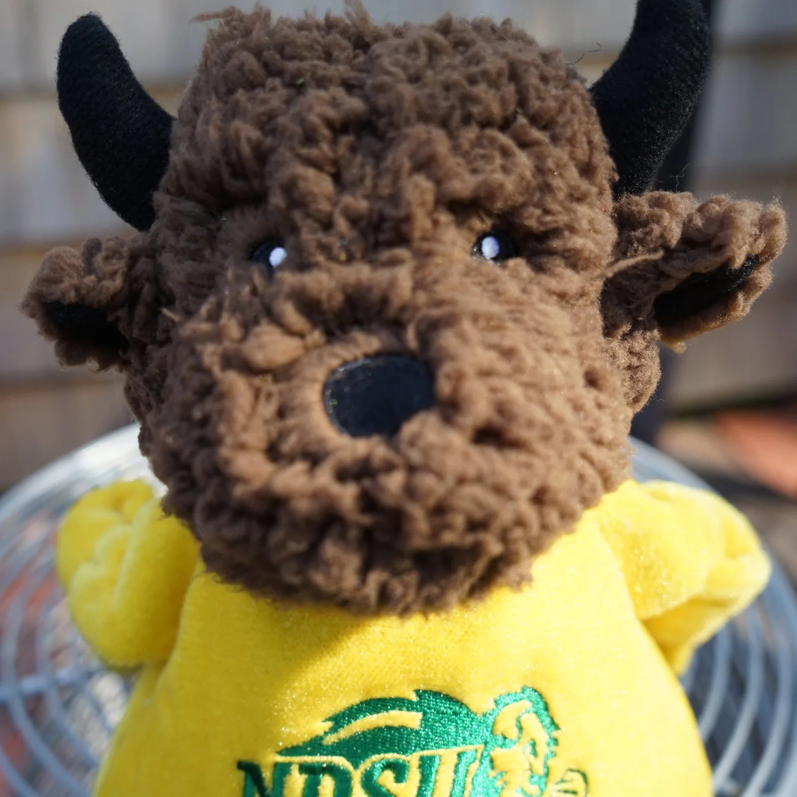 Brown plush bison dog toy wearing a yellow North Dakota State University shirt, featuring knotted limbs and playful expres...