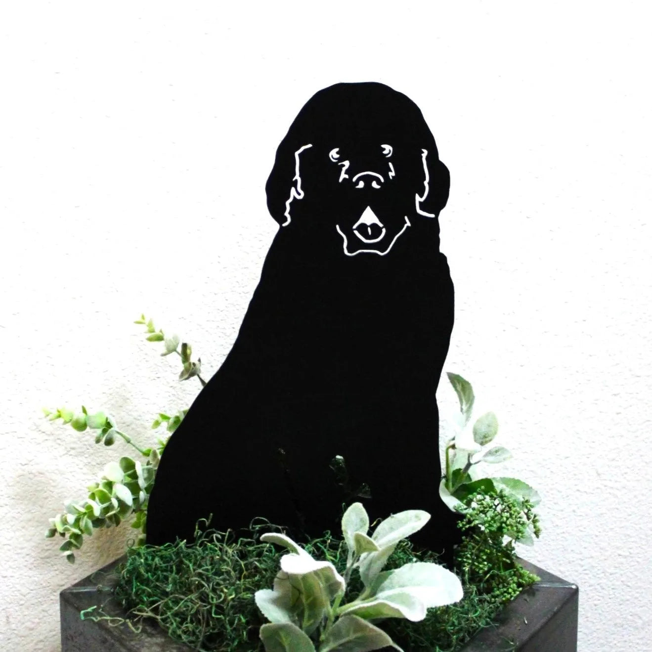Black Newfoundland dog silhouette made of metal, surrounded by greenery, with a simple yet striking design.