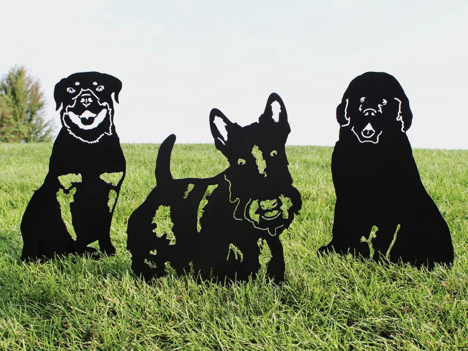 Black metal silhouettes of dog breeds, including a Newfoundland, set against green grass, ideal for outdoor decor.