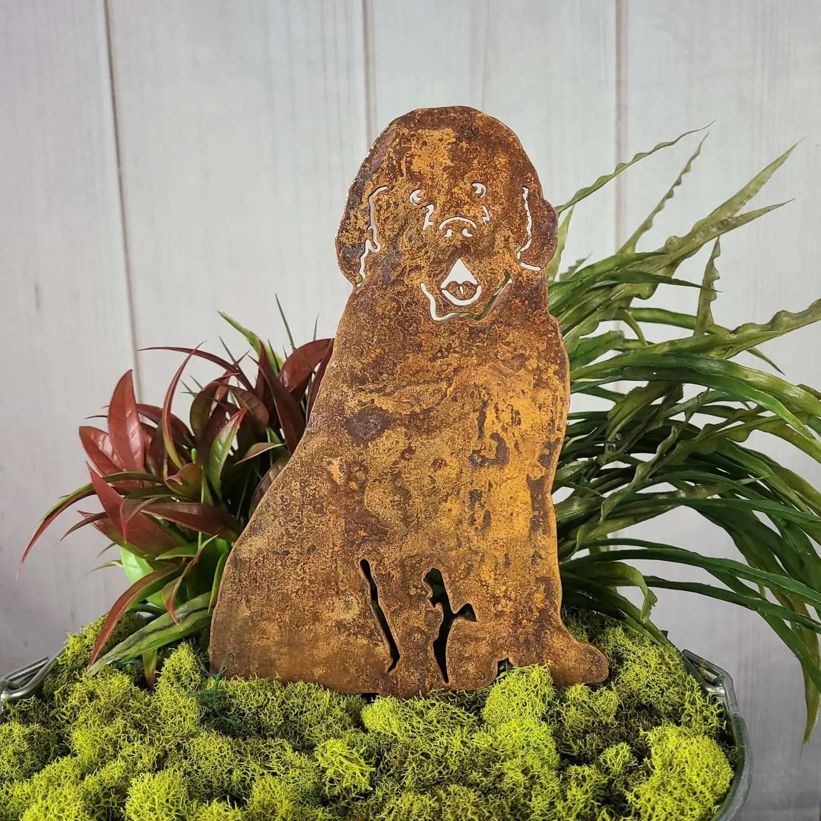 Rustic Newfoundland dog silhouette crafted from weathering steel, nestled among vibrant green moss and foliage.
