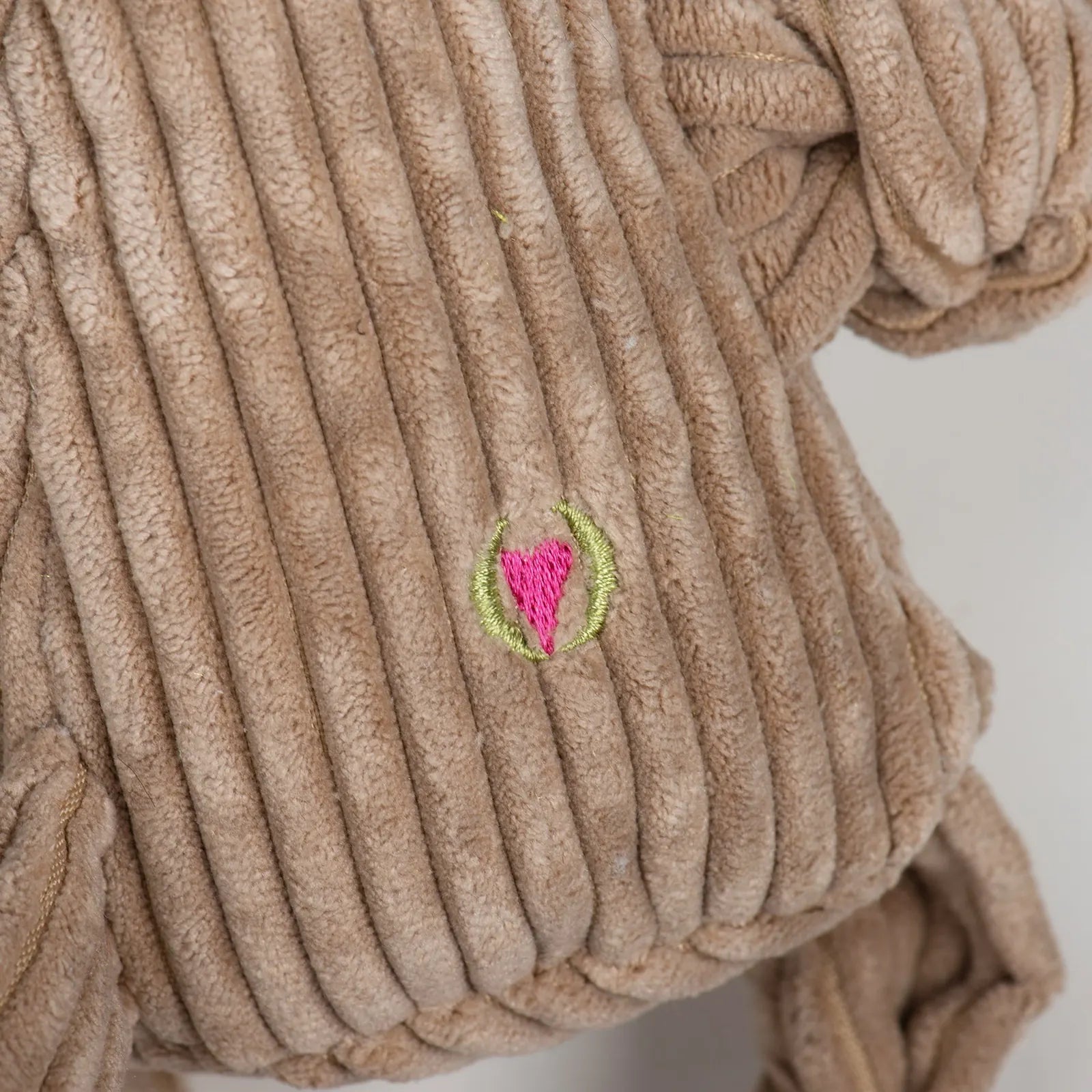 Light brown plush dog toy with ribbed texture, featuring a colorful embroidered heart emblem. Perfect for interactive play.