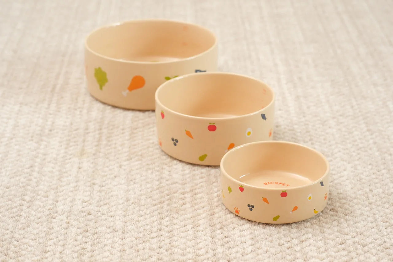 Nomnom Bowl set featuring three sizes in soft beige with colorful food-themed prints, made from durable ceramic.
