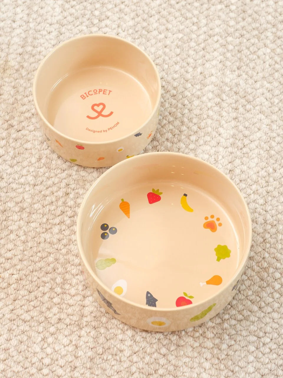 Nomnom Bowl by pehomnyc, featuring colorful food illustrations on a beige ceramic surface, designed for pet feeding.