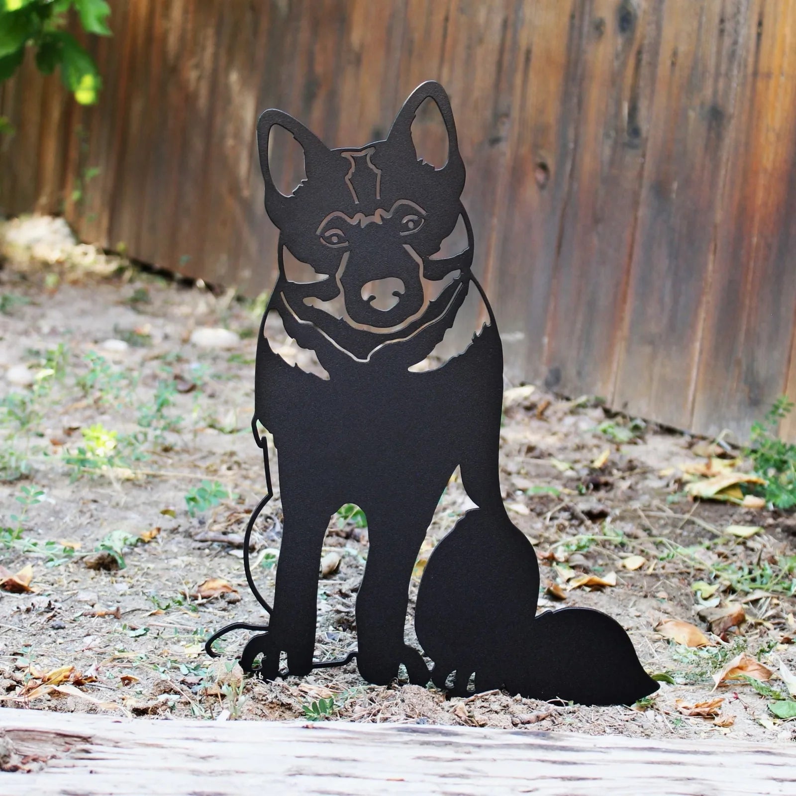 Norwegian Elkhound metal silhouette in matte black, handcrafted, set in a garden with a wooden fence background.