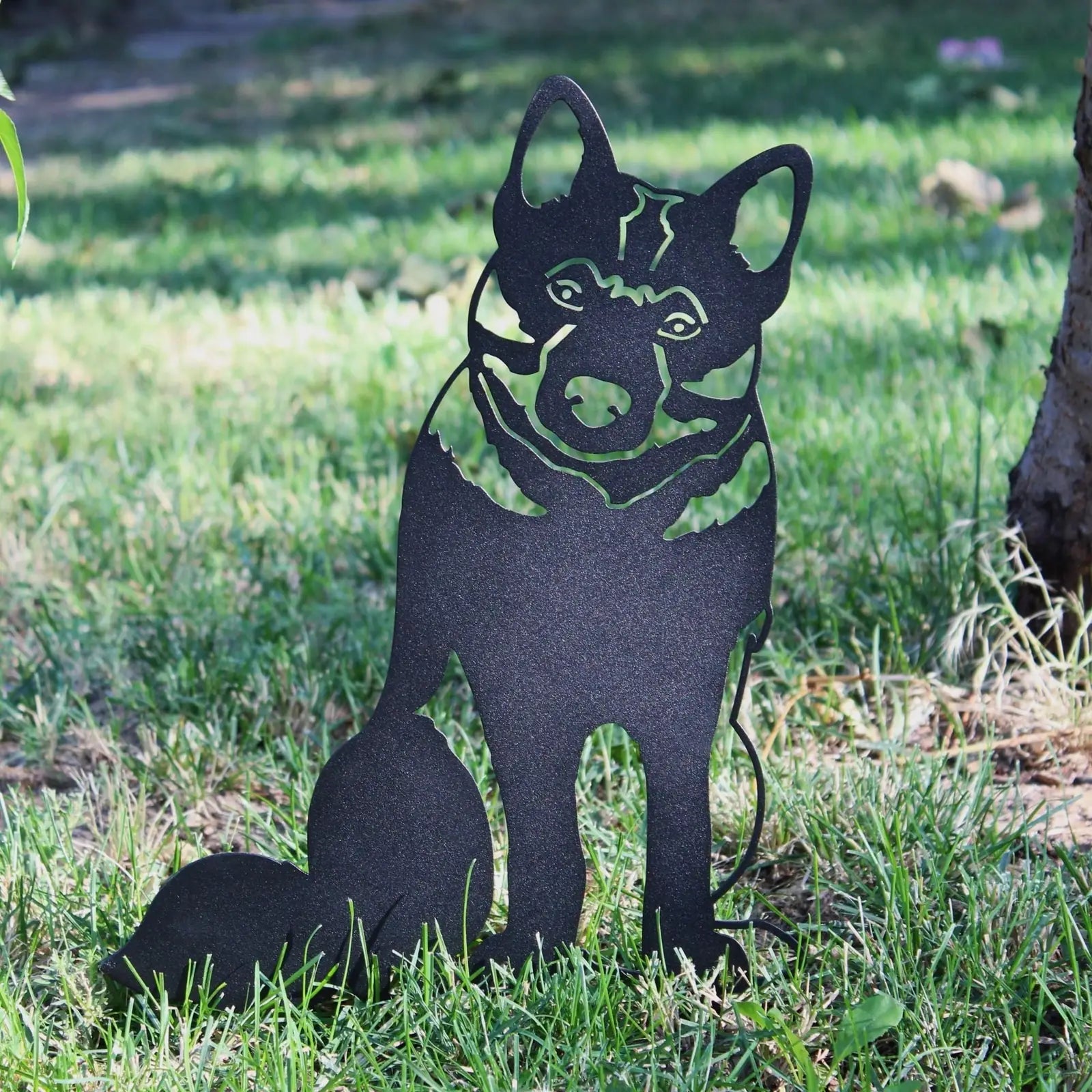 Handmade black metal silhouette of a Norwegian Elkhound sitting on green grass, showcasing fine details and design.