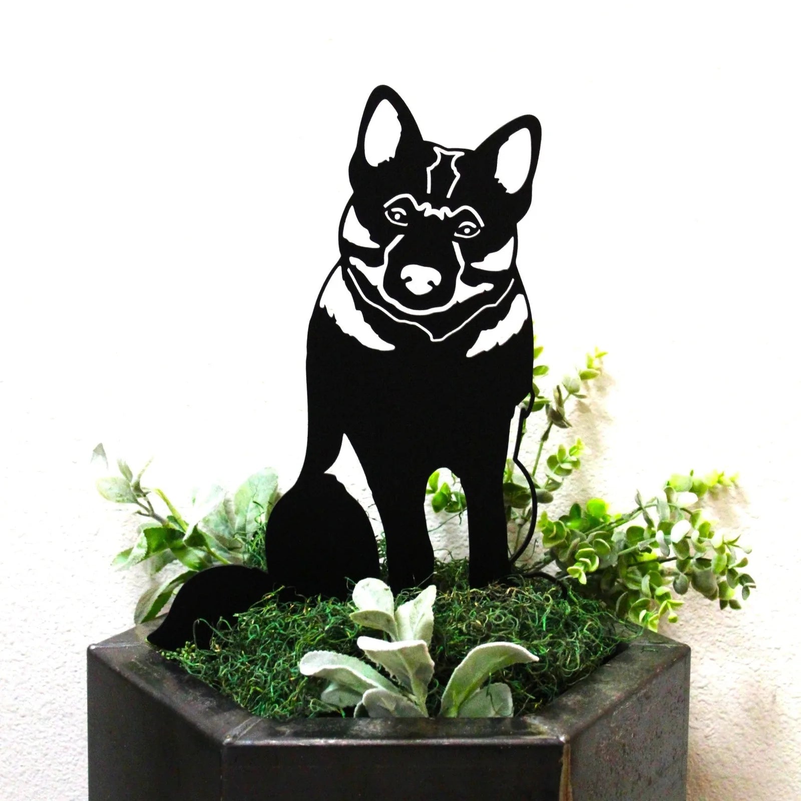 Black metal silhouette of a Norwegian Elkhound, displayed among greenery in a planter.