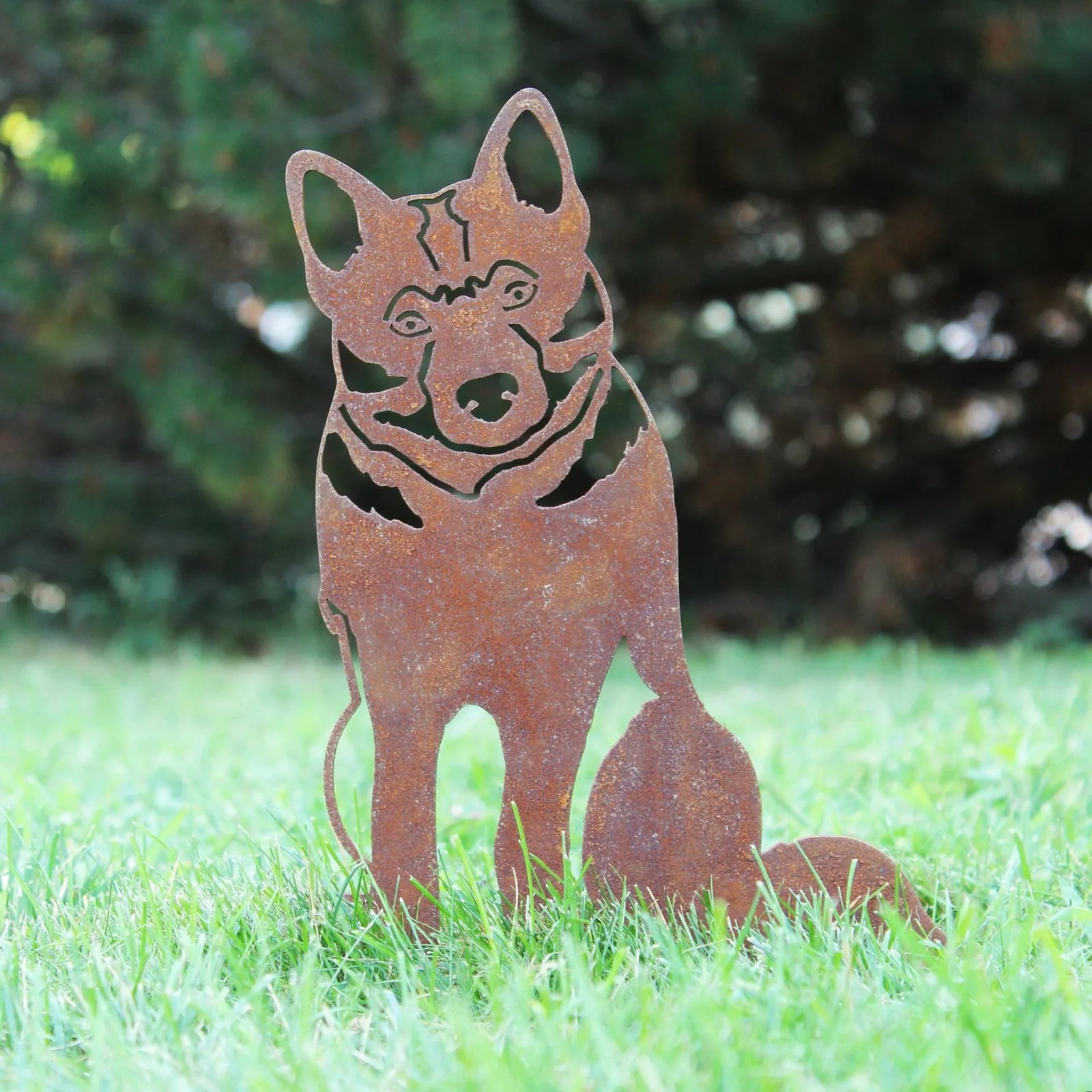 Rusty silhouette of a Norwegian Elkhound dog made of weathering steel, set against green grass and trees.