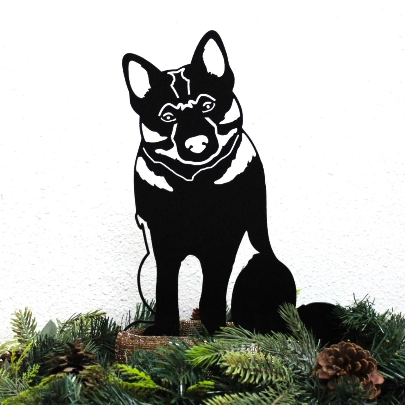 Black metal silhouette of a Norwegian Elkhound seated, surrounded by greenery and pinecones, showcasing outdoor décor.