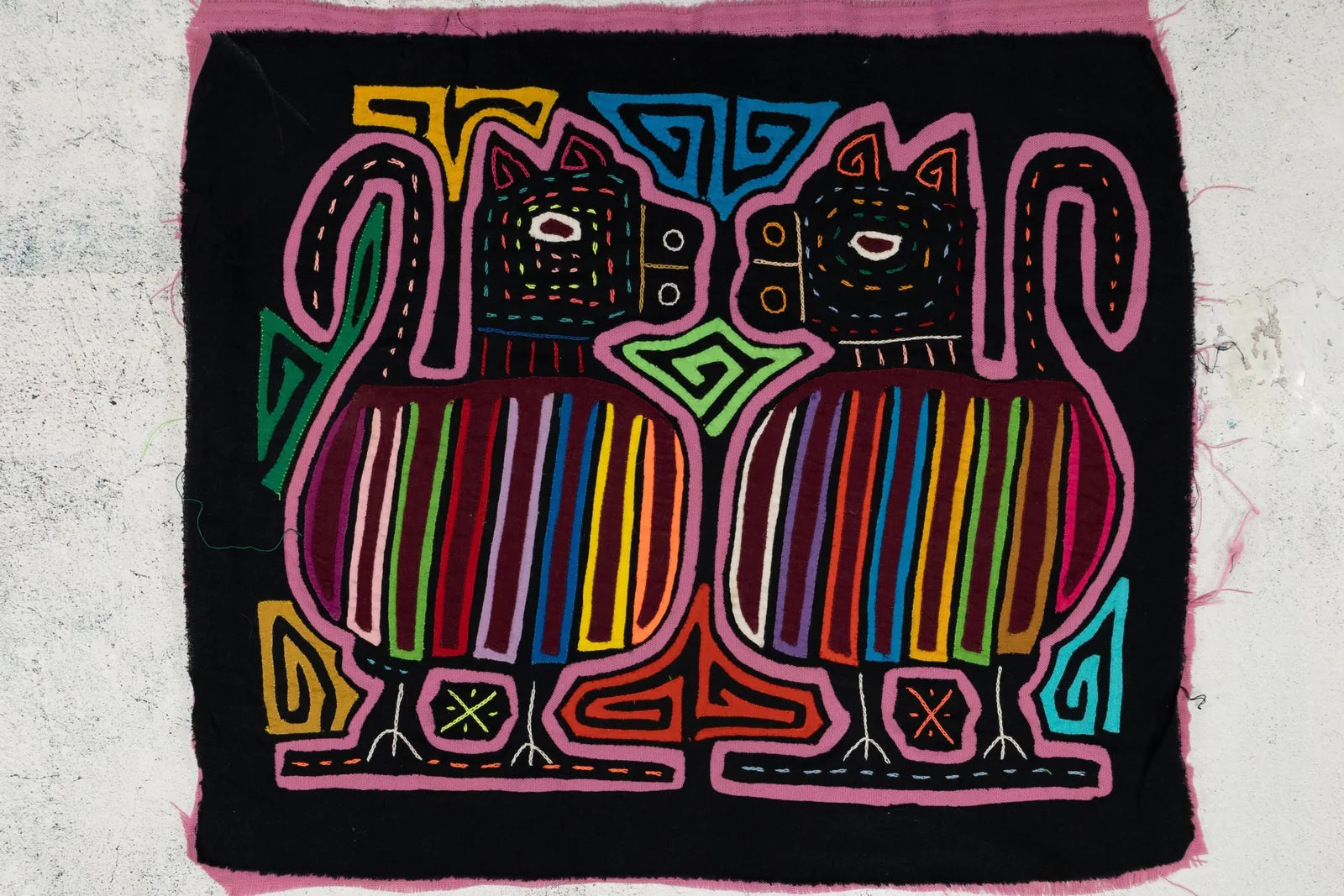 Colorful hand-stitched mola featuring two stylized animals with striped patterns against a black background.
