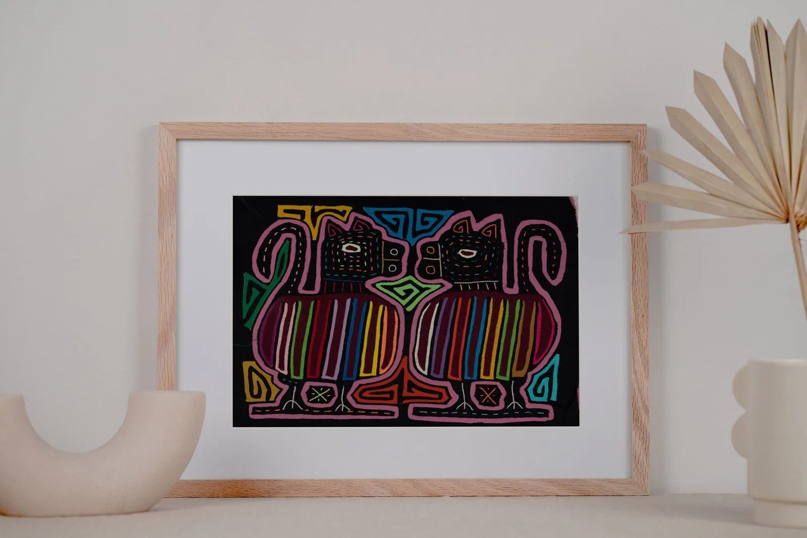 Colorful hand-stitched Mola featuring two stylized dogs with geometric patterns, framed and displayed on a minimalistic sh...