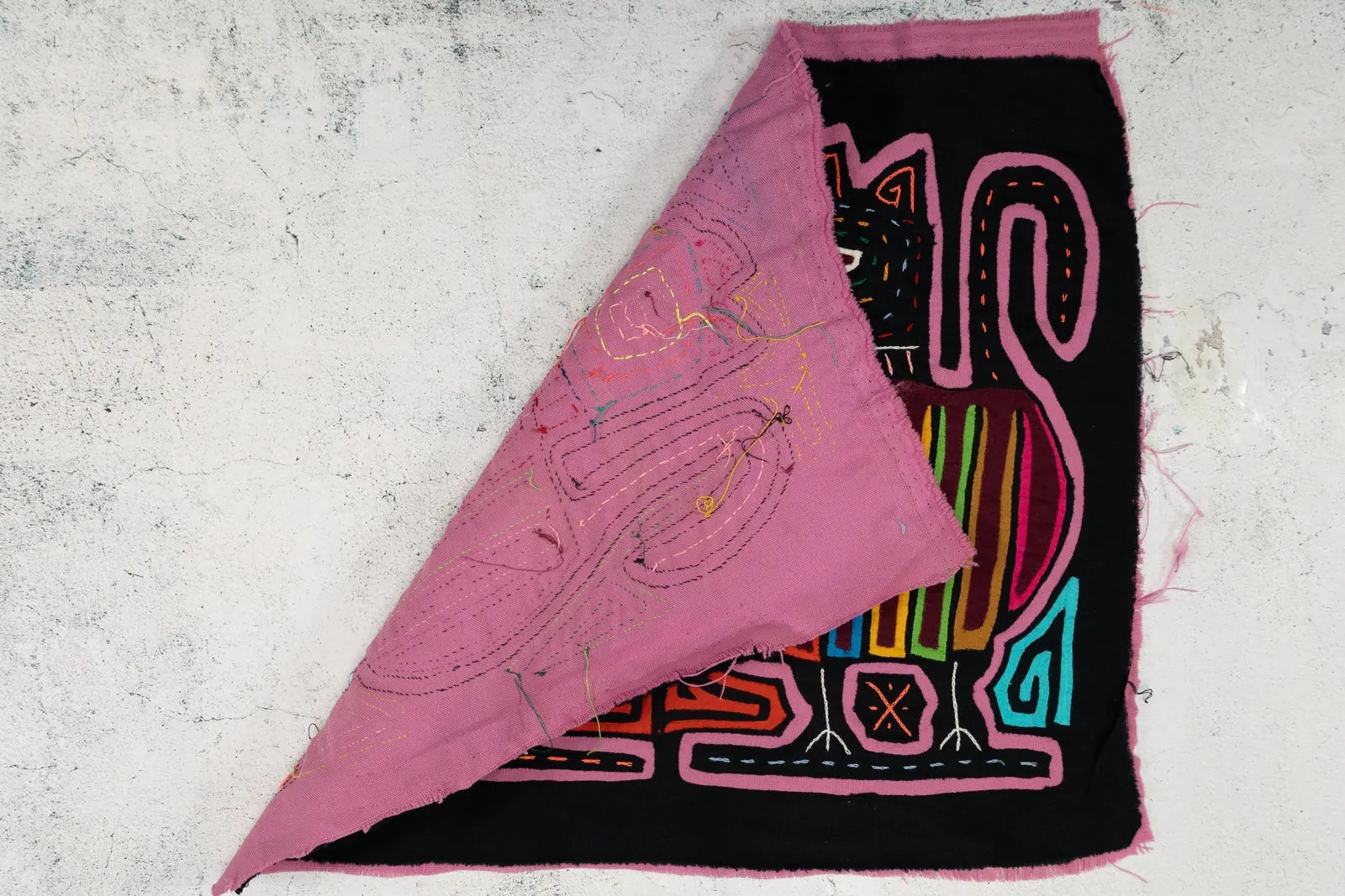 Colorful hand-stitched puppy design on vibrant Mola textile with intricate patterns and a black background.