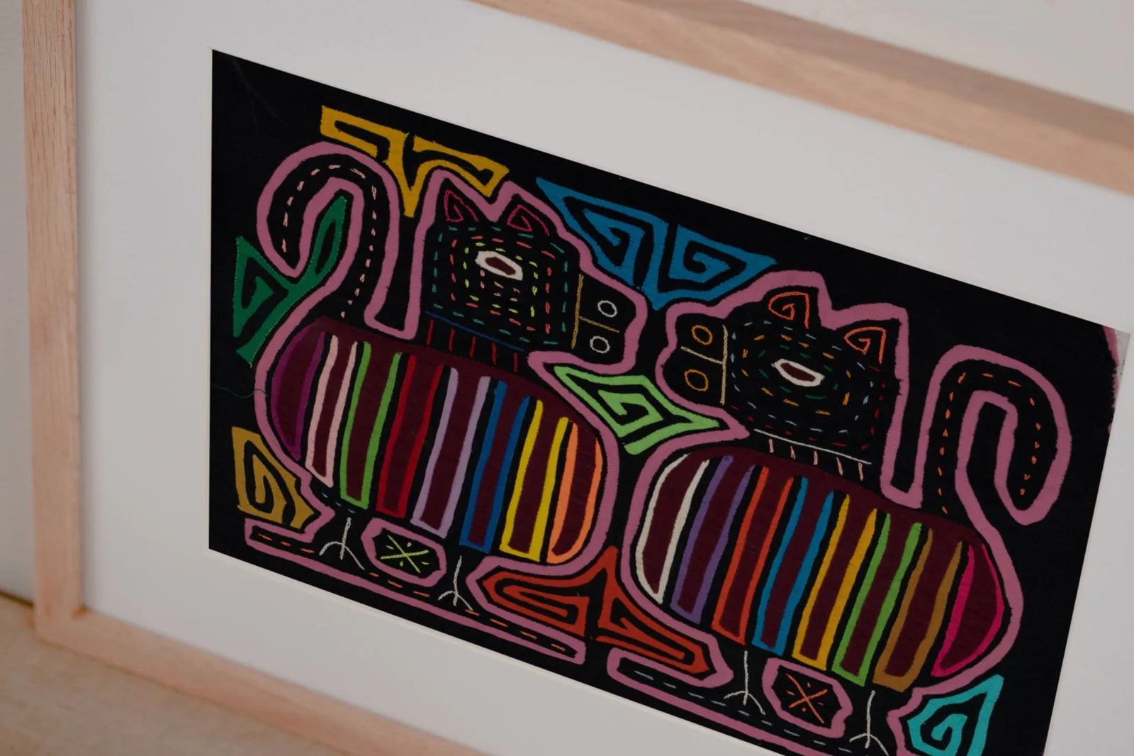 Hand-stitched Mola featuring two colorful, stylized dog figures on a black background, framed elegantly.
