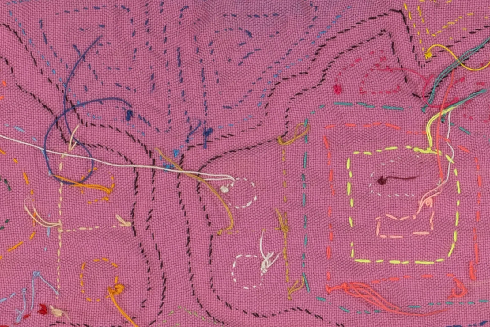 Hand-stitched pink textile featuring colorful geometric patterns and contrasting threads in a Mola design.