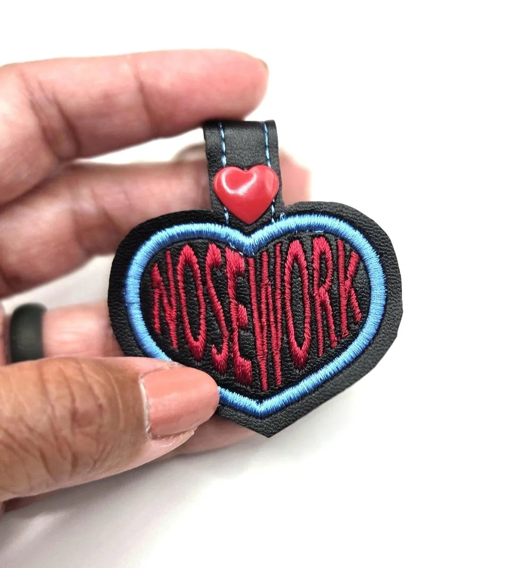 Embroidered heart-shaped keychain featuring "NOSEWORK" in red, bordered by light blue and a red heart accent.