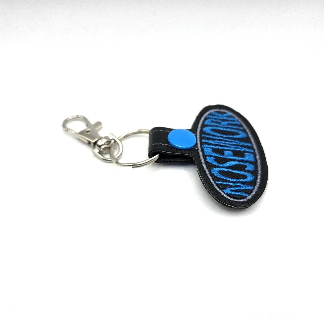 Embroidered keychain featuring "NOSE WORK" in bold blue on a black fob, with a swivel clip for easy attachment.