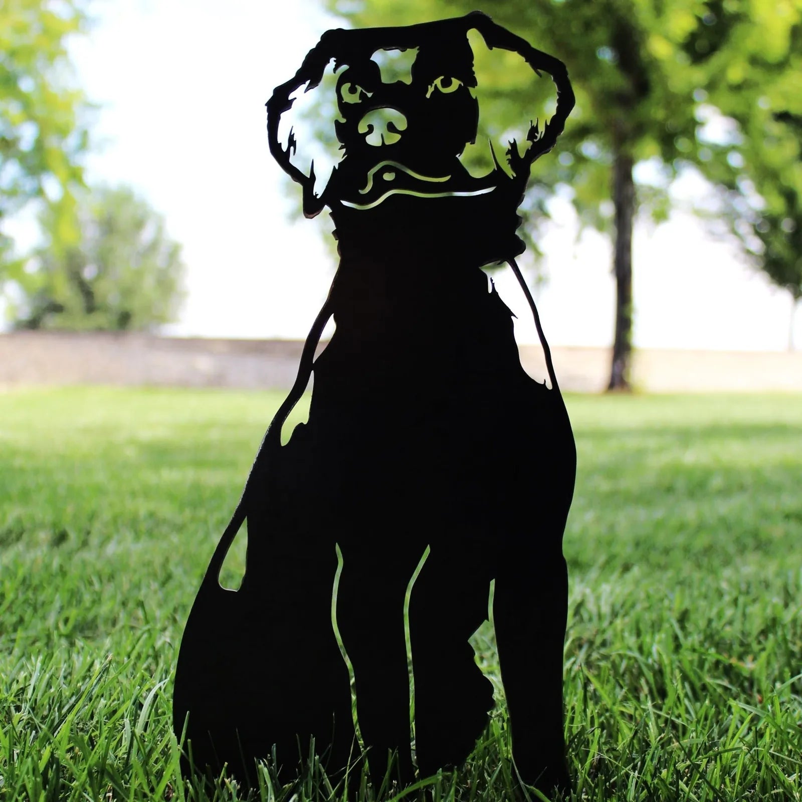 Nova Scotia Duck Tolling Retriever metal silhouette in matte black, set against green grass and trees outdoors.