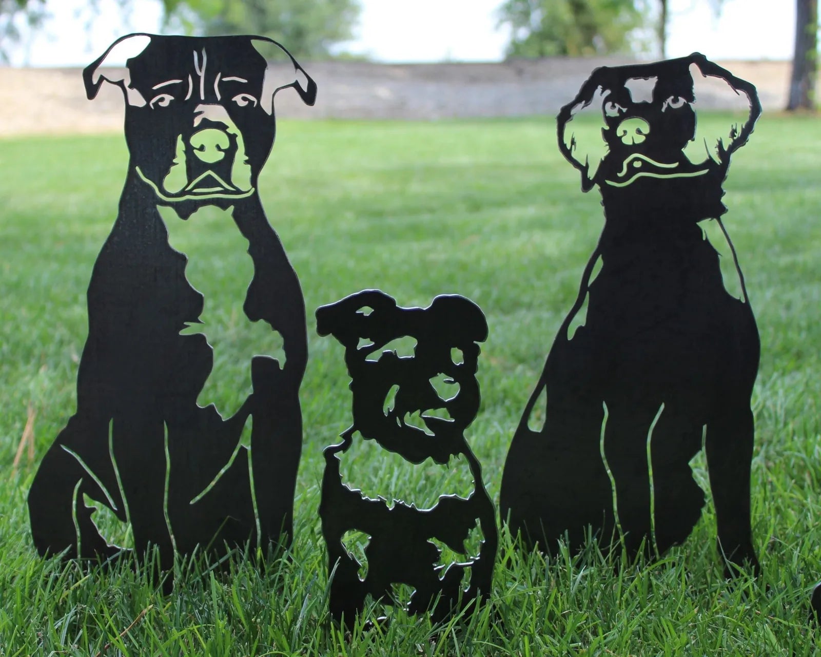 Black metal silhouettes of three dogs, including a Nova Scotia Duck Tolling Retriever, displayed on green grass.