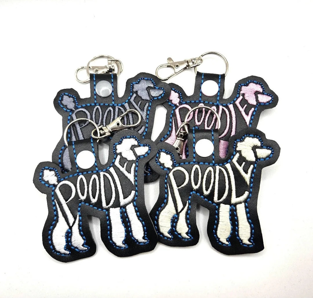 Four Poodle-shaped keychains in black, gray, and pink with "POODLE" embroidered, featuring swivel lobster clasps.