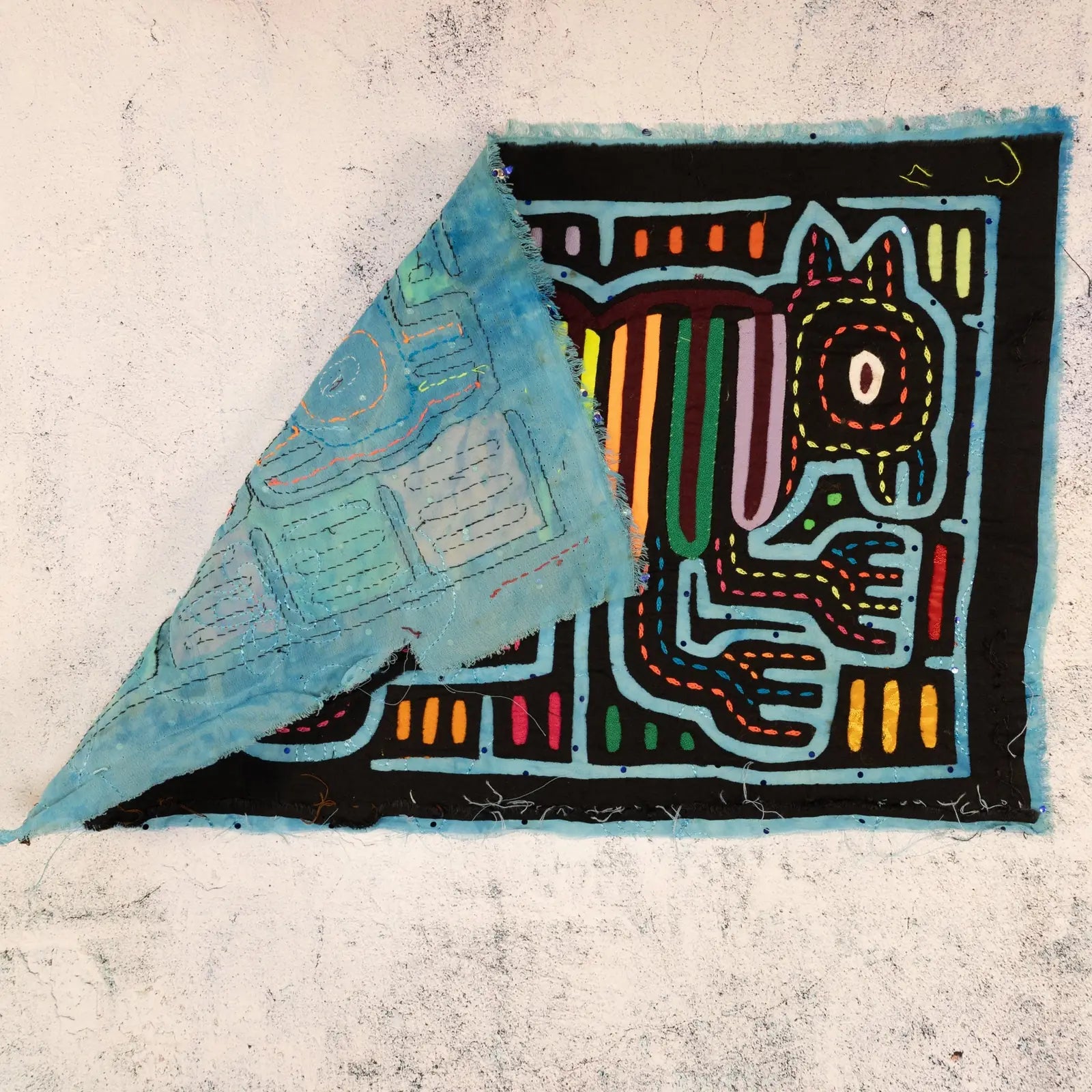 Colorful hand-stitched Mola textile art featuring two dogs, showcasing intricate patterns and vibrant colors on a black ba...