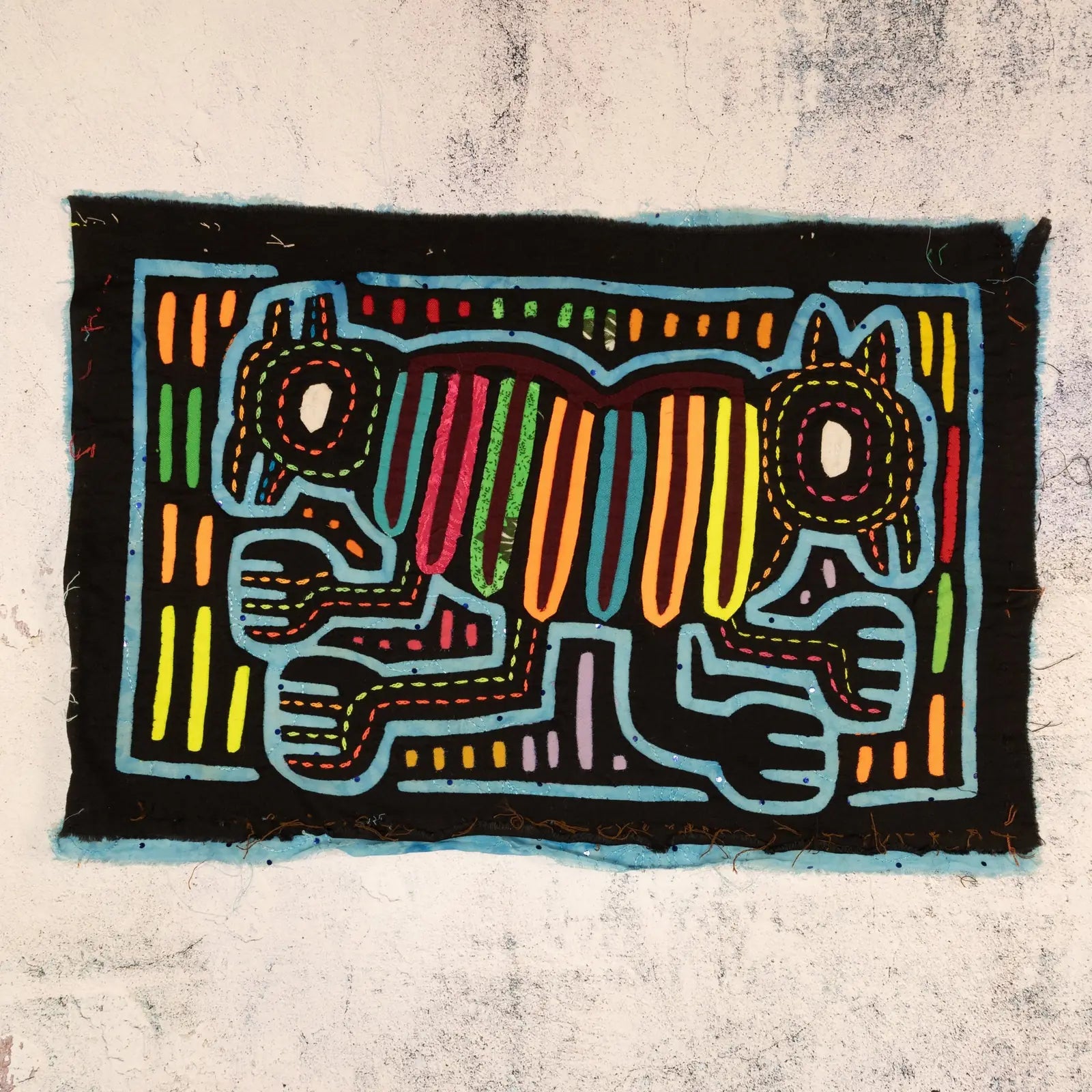 Colorful hand-stitched Mola tapestry featuring a geometric optical illusion design of two dogs on a black background.