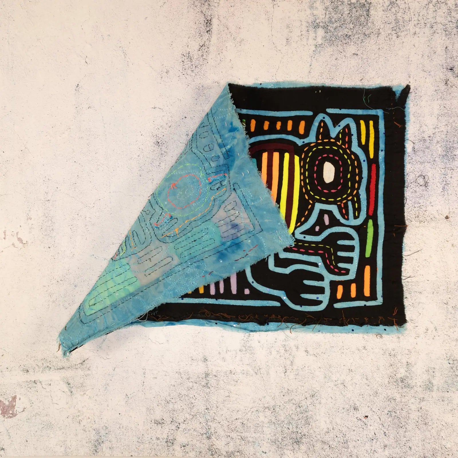 Hand-stitched Mola tapestry featuring vibrant colors and intricate designs of dogs on a black background with blue accents.