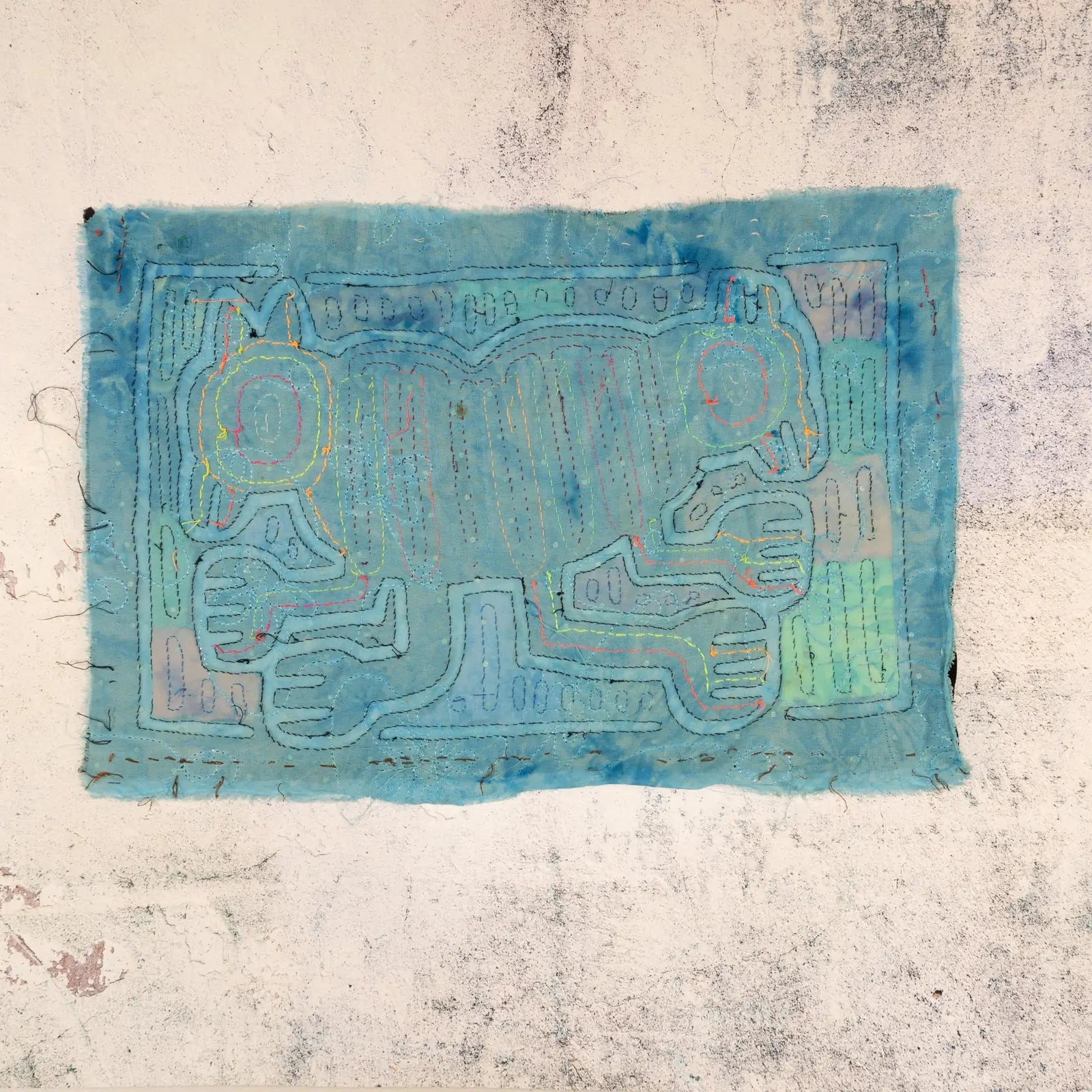 Intricate blue hand-stitched Mola textile art featuring a symmetrical dog design with vibrant detailing.