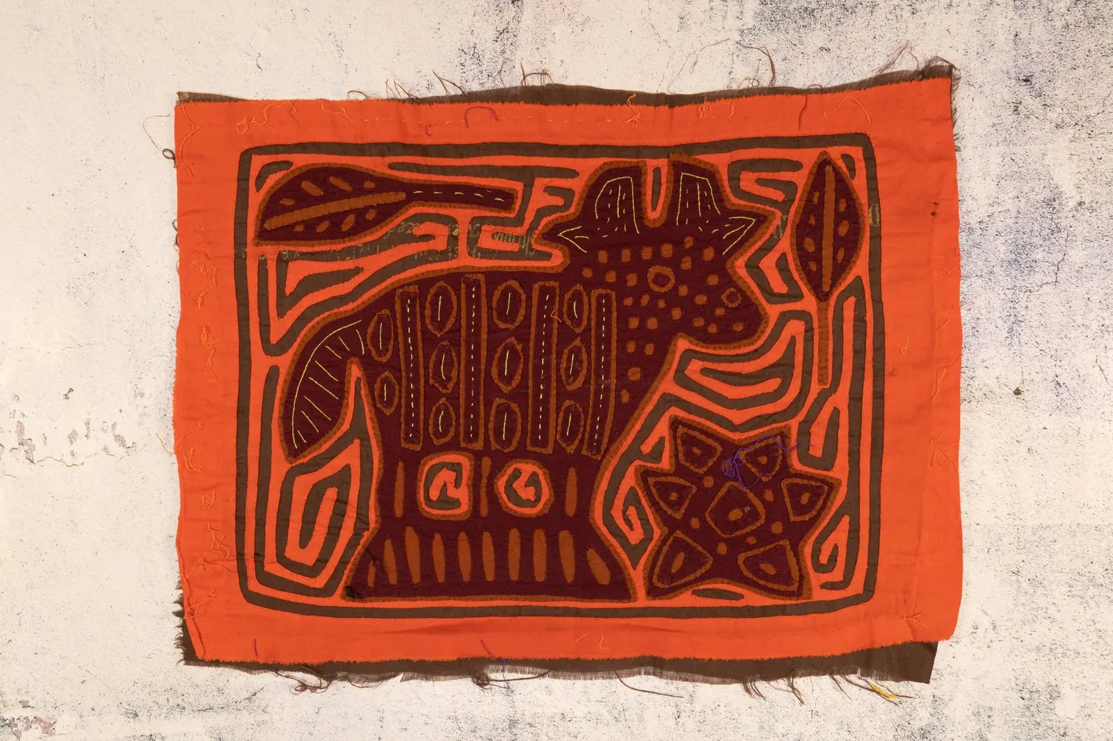 Hand-stitched orange and brown Mola tapestry featuring a puppy design with geometric patterns.