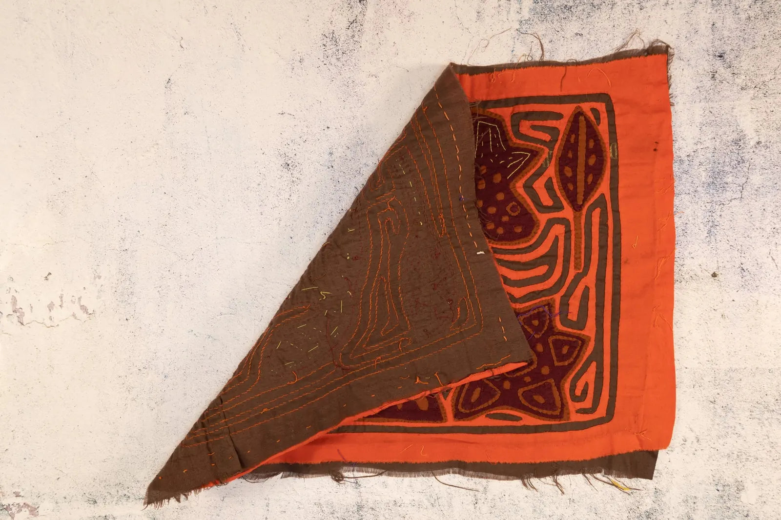 Hand-stitched orange and brown Mola tapestry featuring geometric patterns and layered fabrics. Fair Trade from Panama.