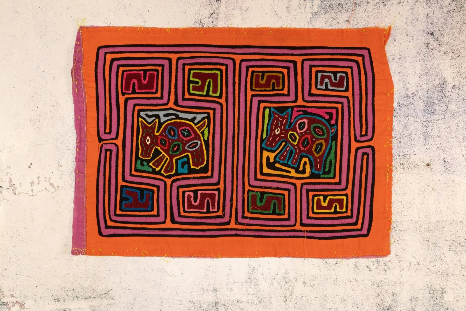 Colorful orange and purple Mola featuring geometric patterns and puppy dog designs, handmade by indigenous artisans.