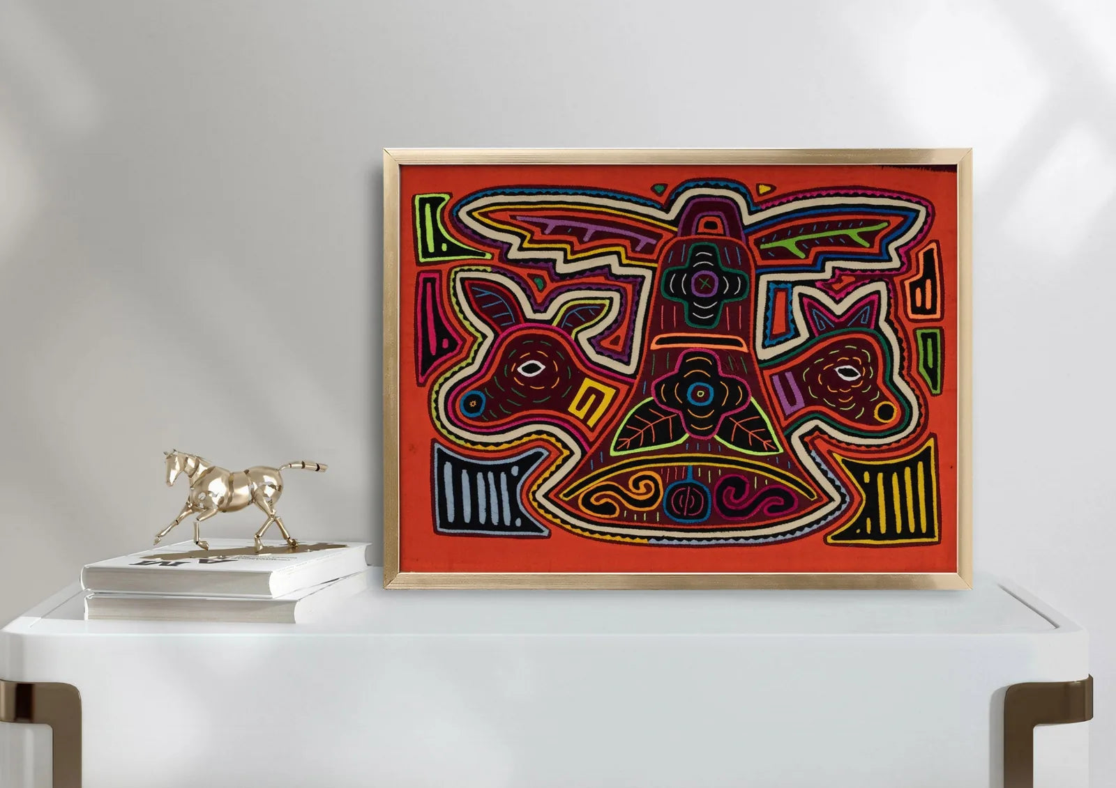 Hand-stitched orange and white puppy Mola tapestry with bold patterns, framed and displayed on a white table.