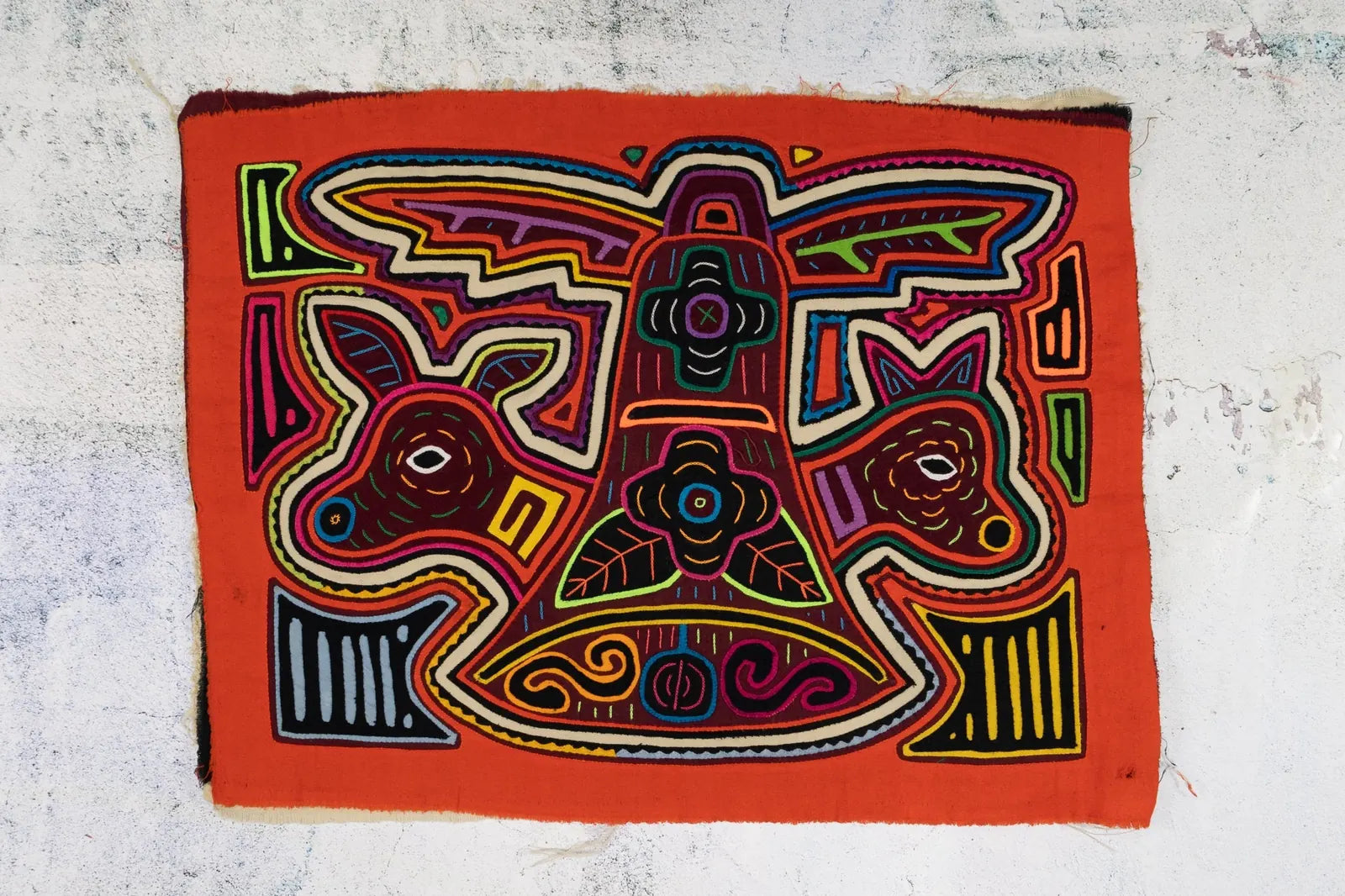 Colorful hand-stitched orange and white puppy design on a vibrant orange tapestry, showcasing intricate patterns and shapes.