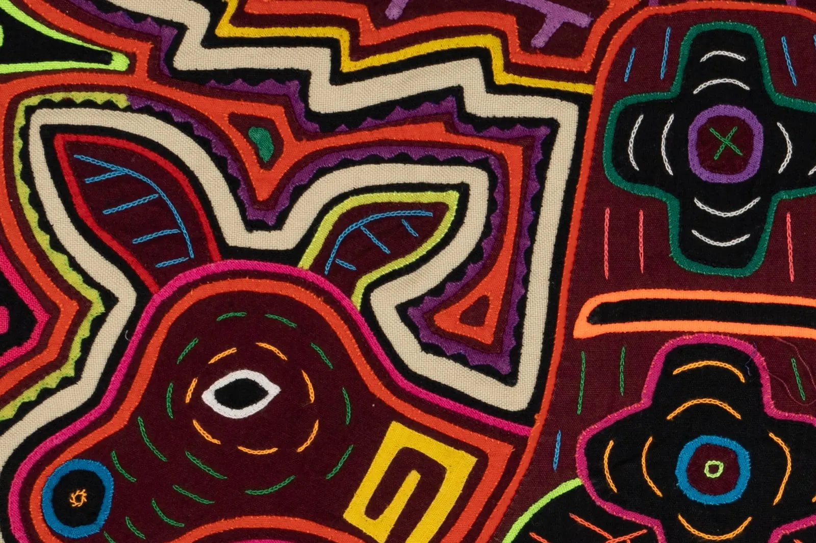 Colorful hand-stitched Mola featuring an orange and white puppy dog design with intricate patterns on a dark background.