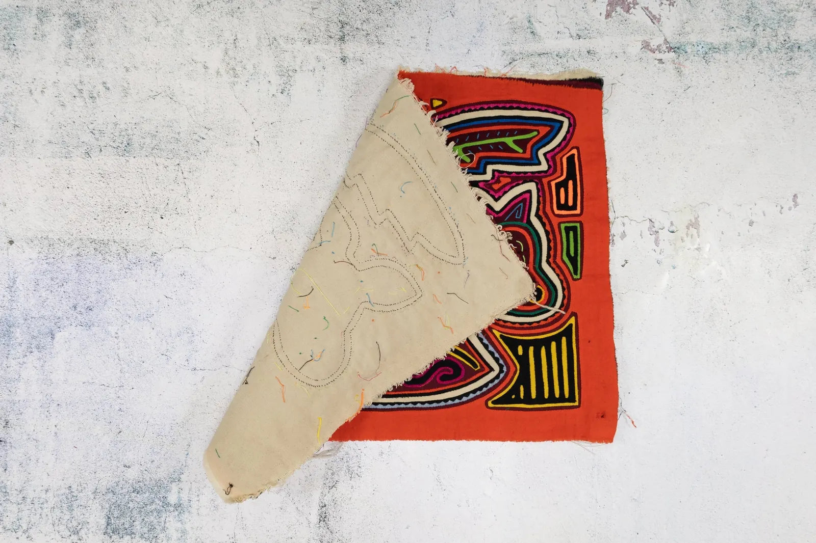 Hand-stitched orange and white puppy Mola tapestry partially folded, showcasing vibrant colors and intricate designs.