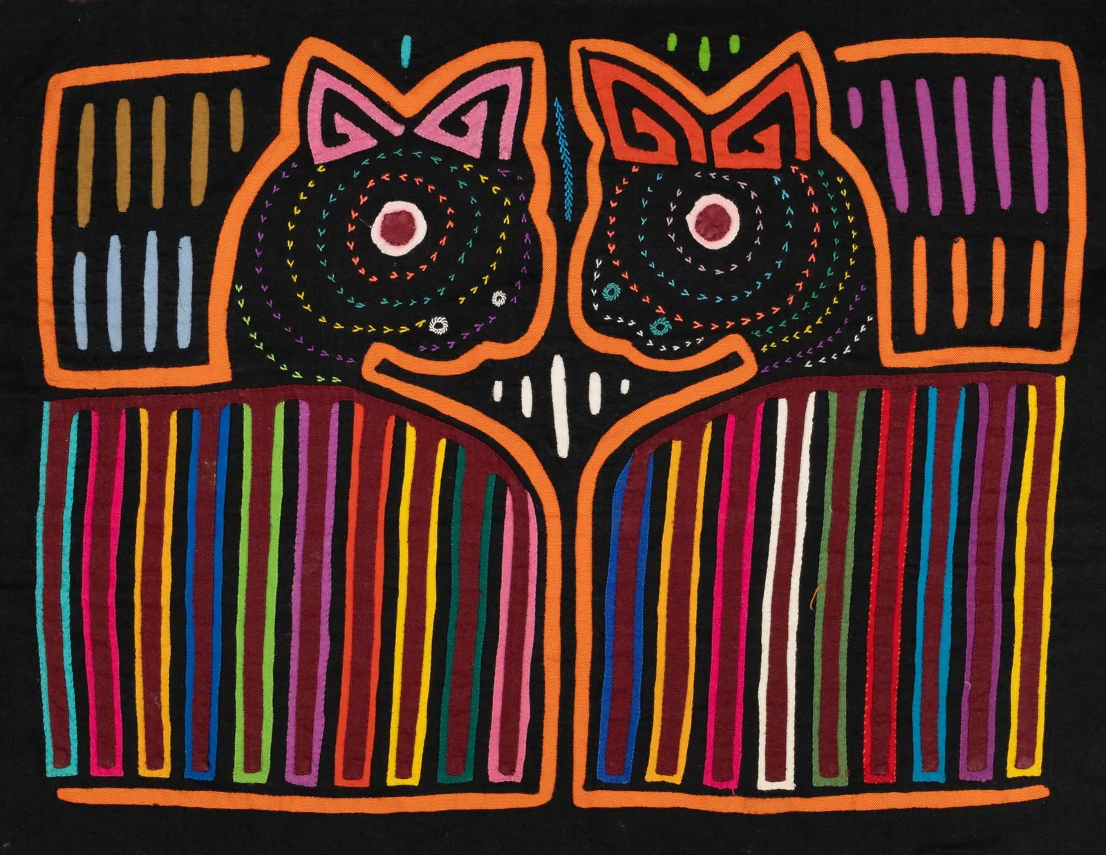 Colorful hand-stitched Mola tapestry featuring two stylized dog faces with geometric patterns on a black background.