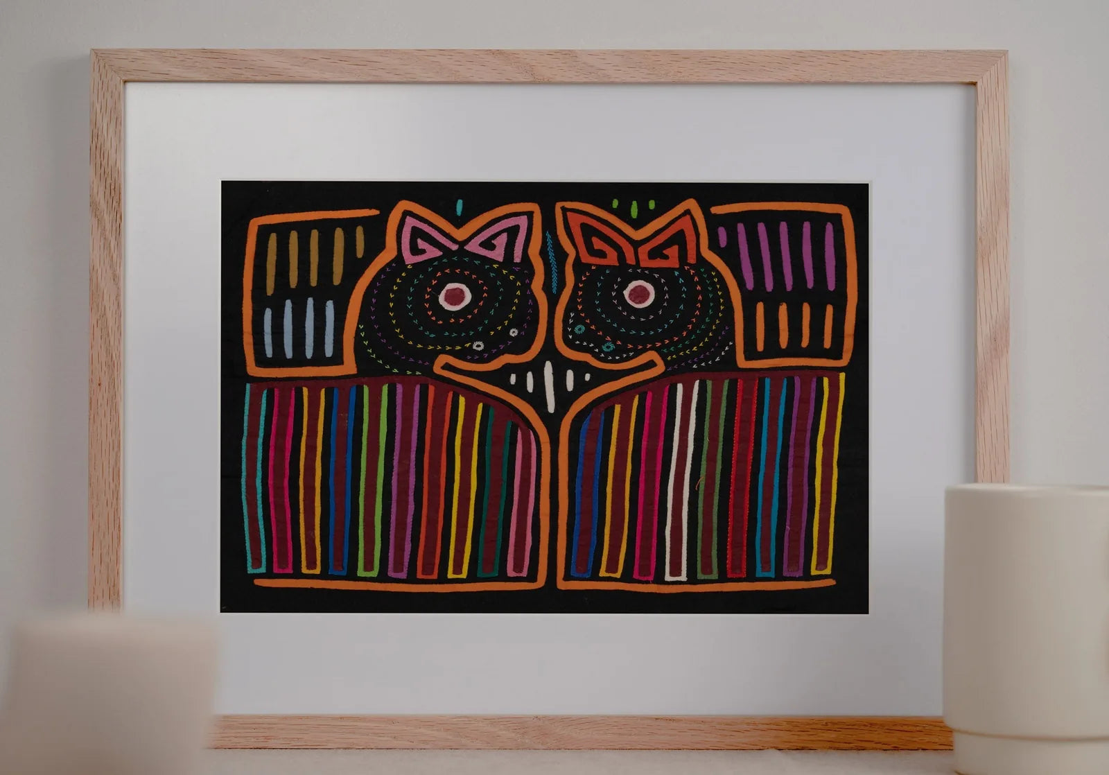 Hand-stitched orange and black Mola tapestry featuring two stylized puppy heads with vibrant geometric patterns.