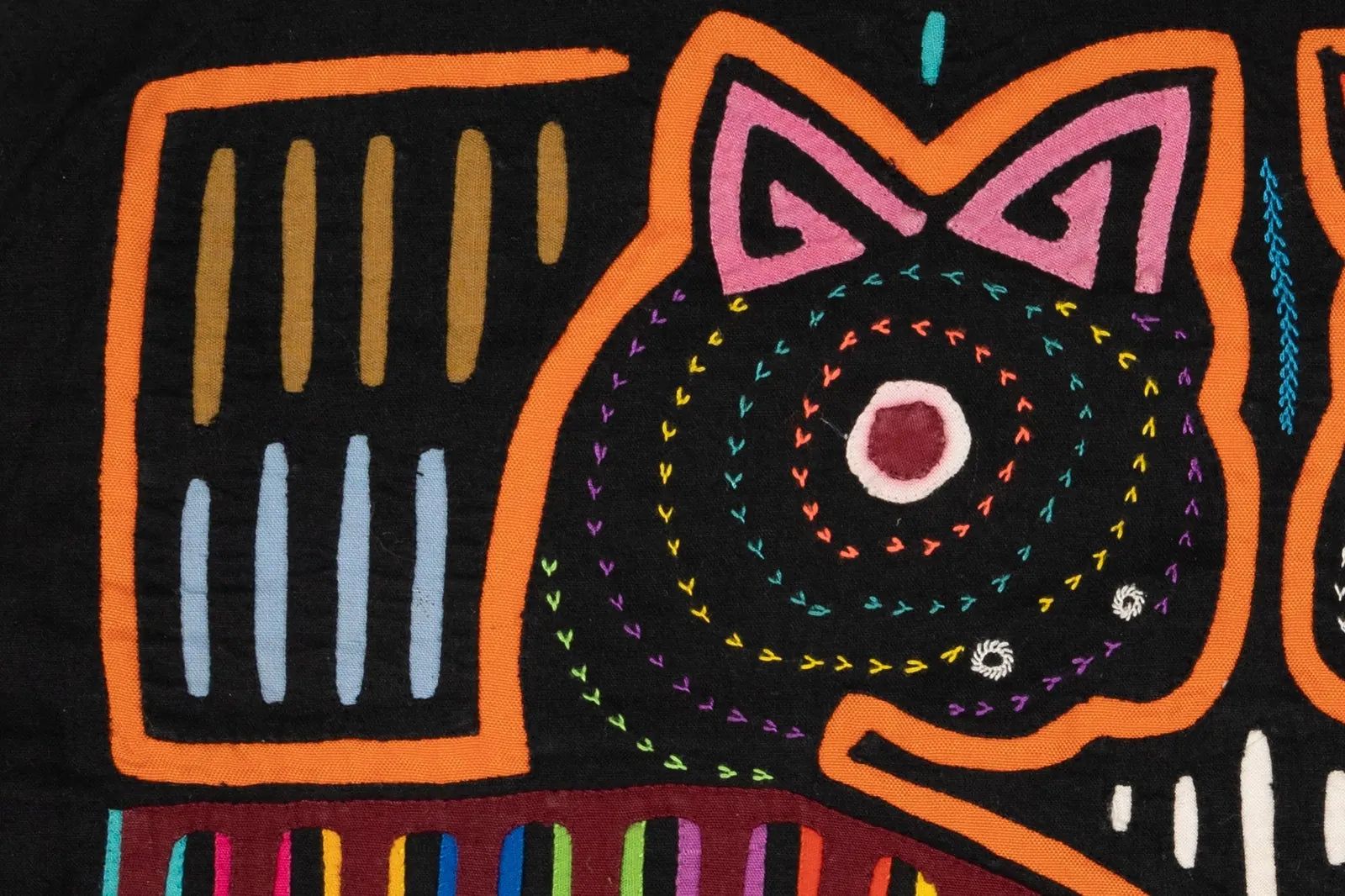 Colorful hand-stitched orange and purple dog design with spiral patterns on a black textile background.